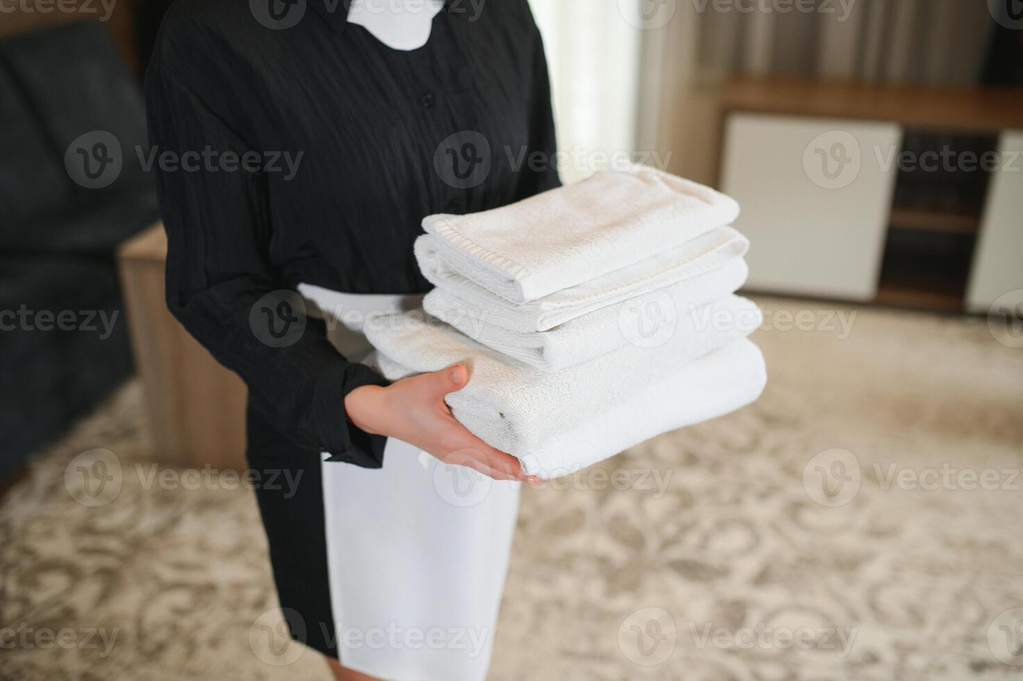 Maid holding fresh towels with flowers in hotel room, closeup photo