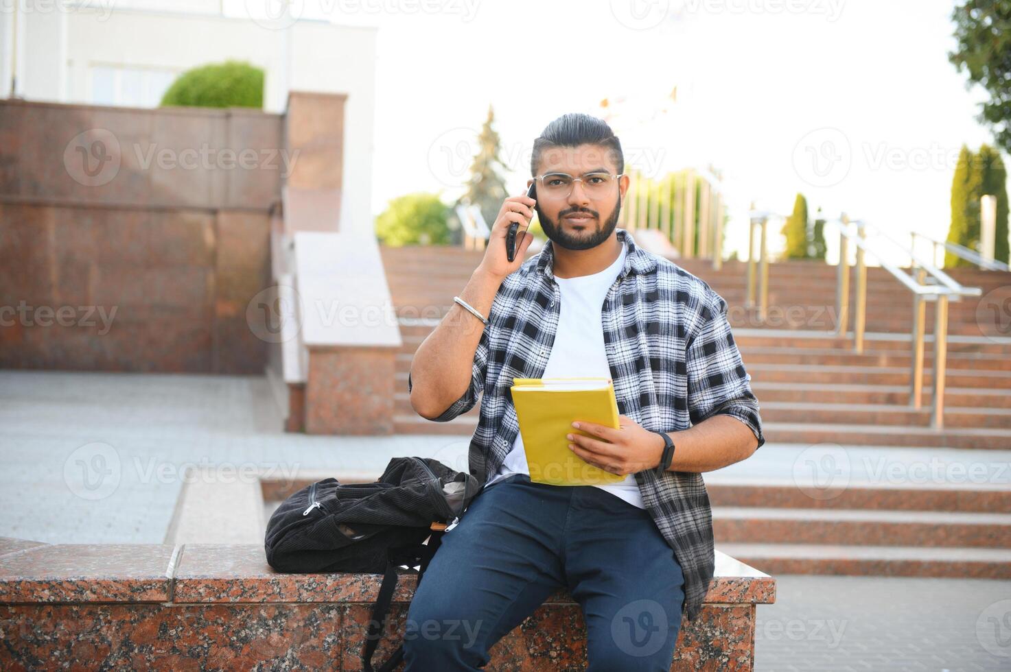 Young Indian male student using mobile phone, standing outside on street photo