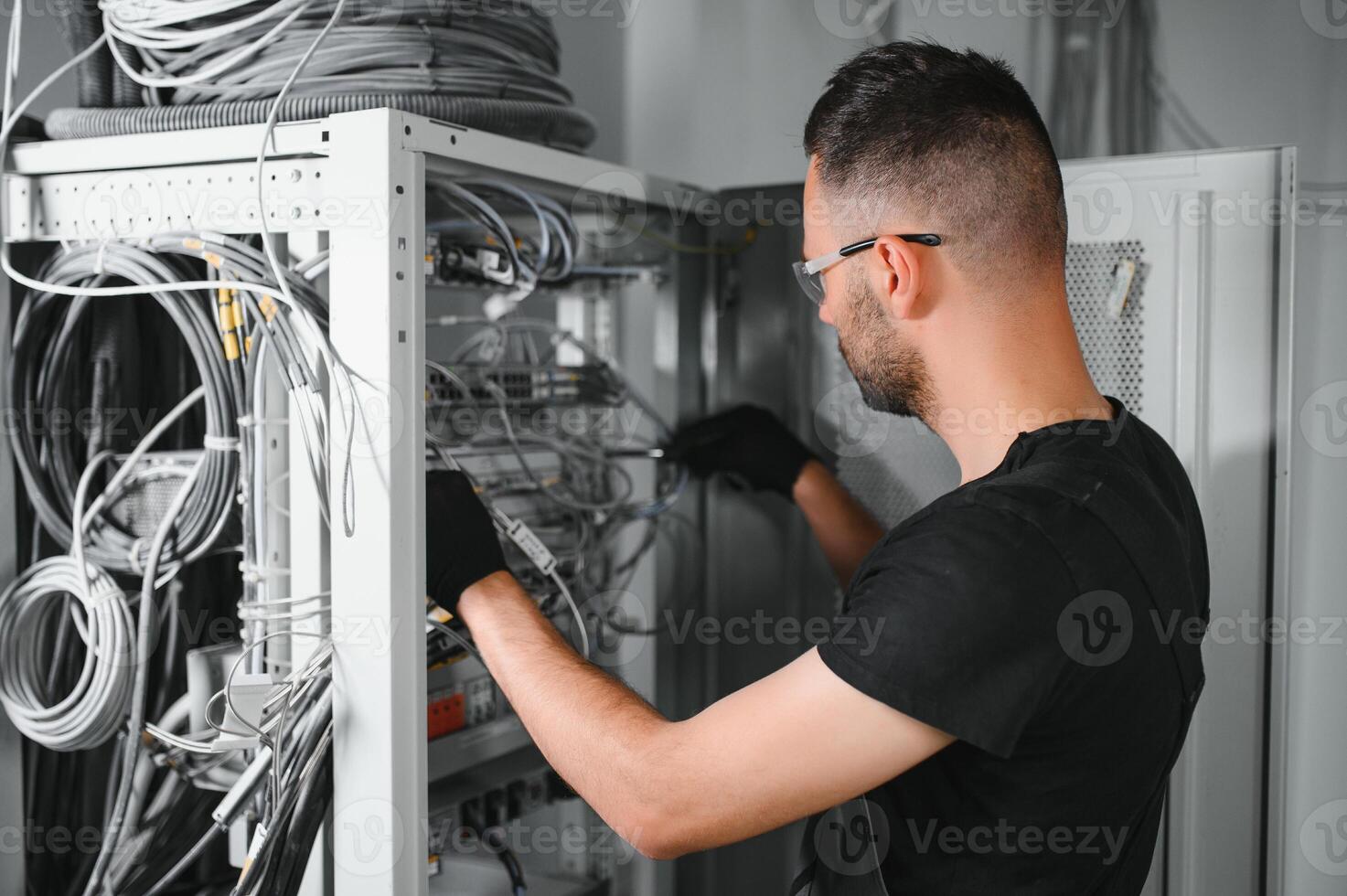 A technician works with server equipment in a data center. A man commutes wires in a server room photo