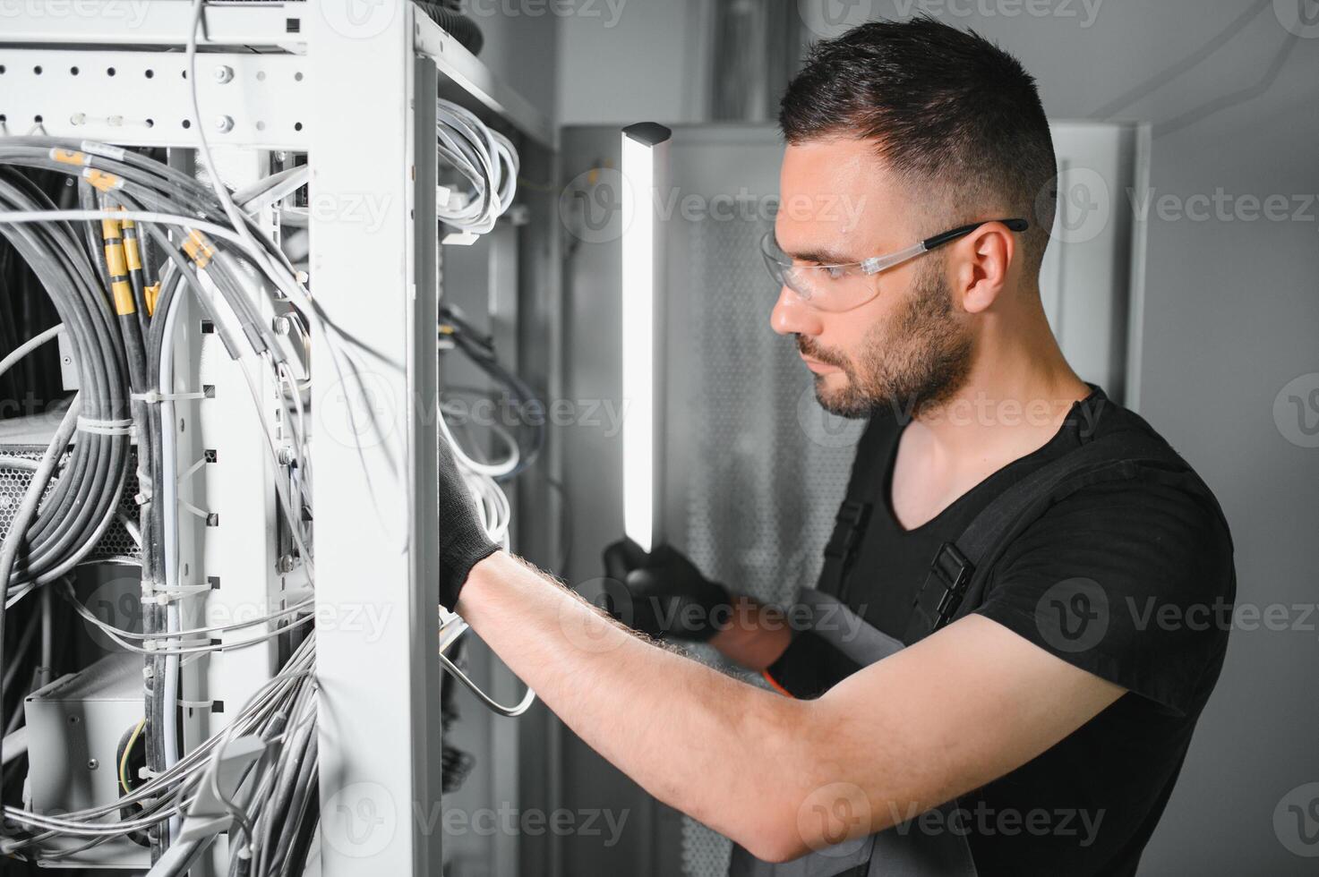 Young man is working with internet equipment and wires in server room photo