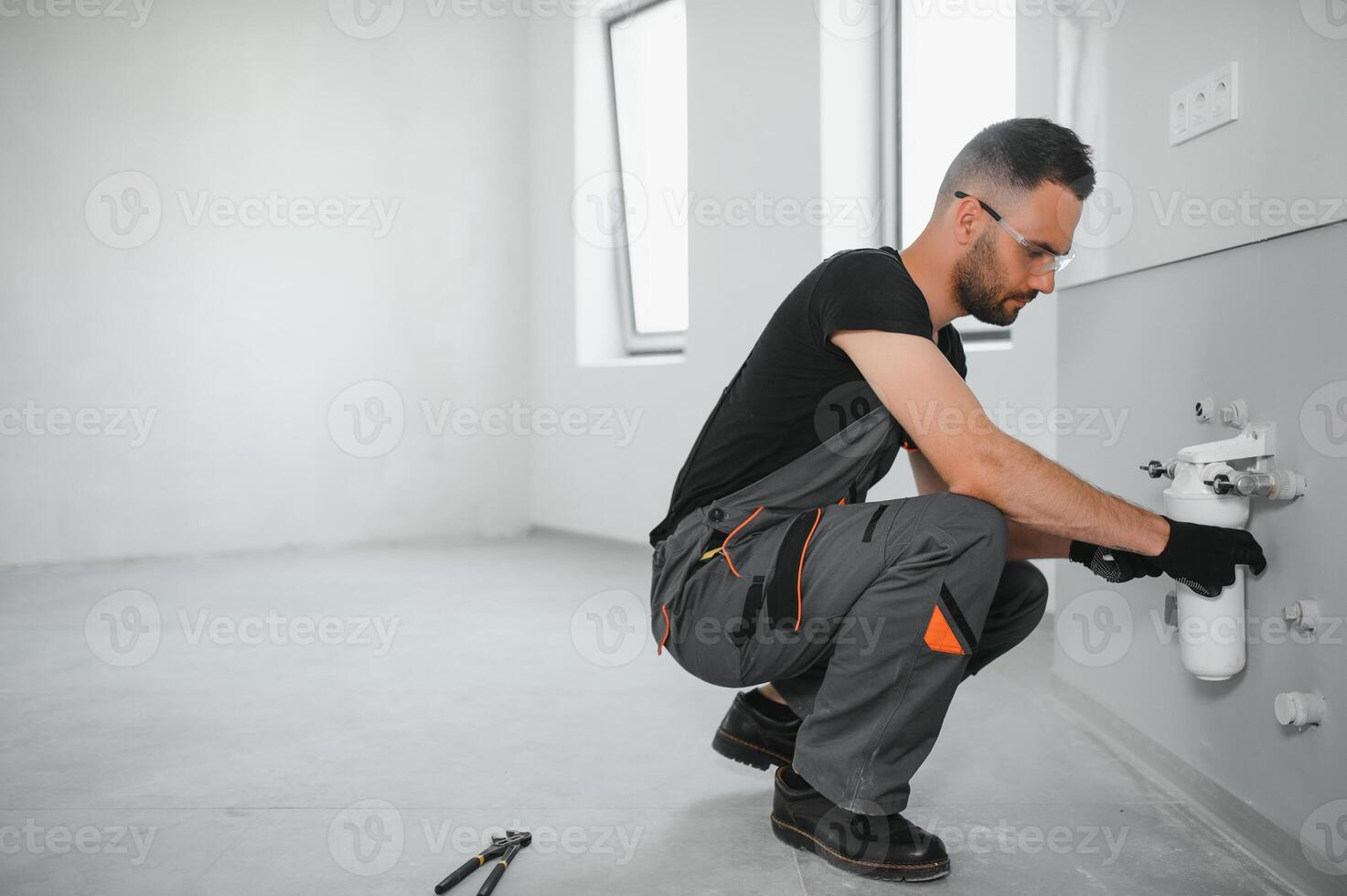 Young man in workwear using pliers while installing water filtration system photo