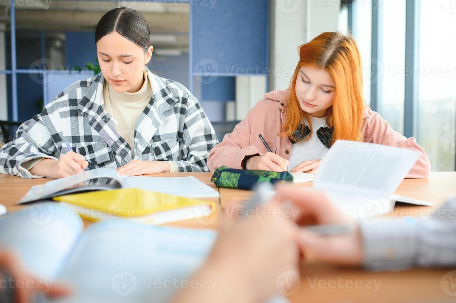 students sit at shared desk making notes studying together at university photo