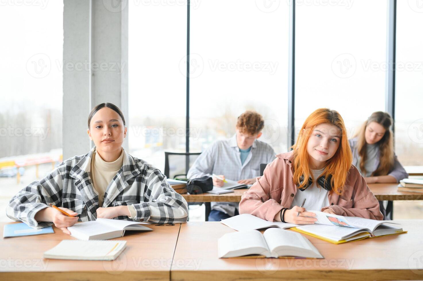students sit at shared desk making notes studying together at university photo