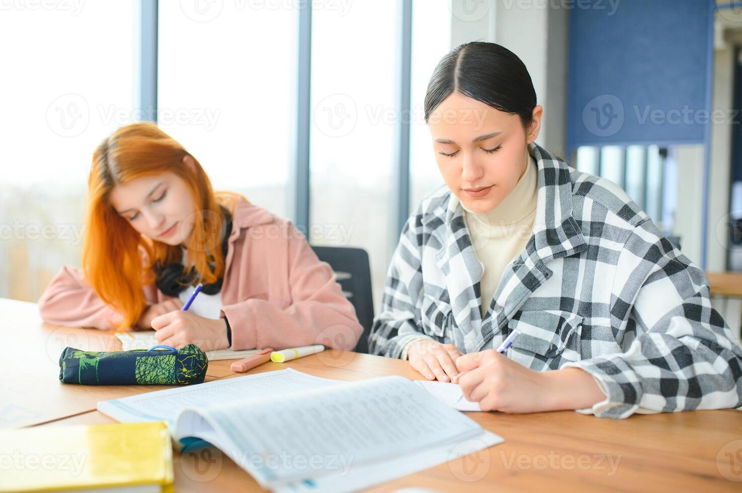 students sit at shared desk making notes studying together at university photo