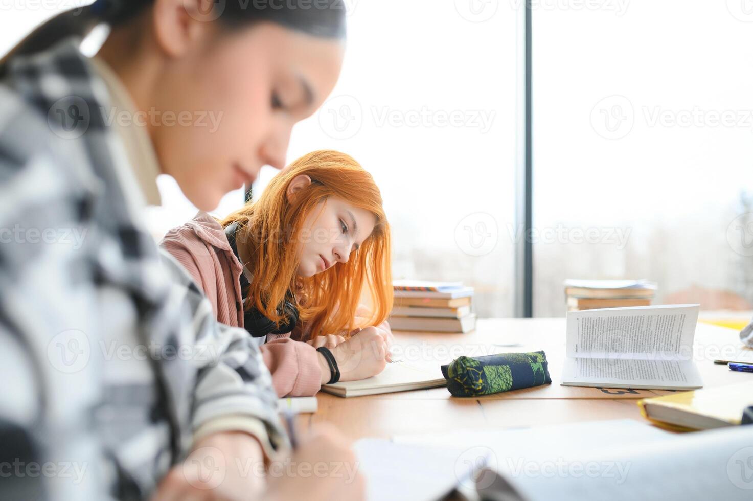 students sit at shared desk making notes studying together at university photo