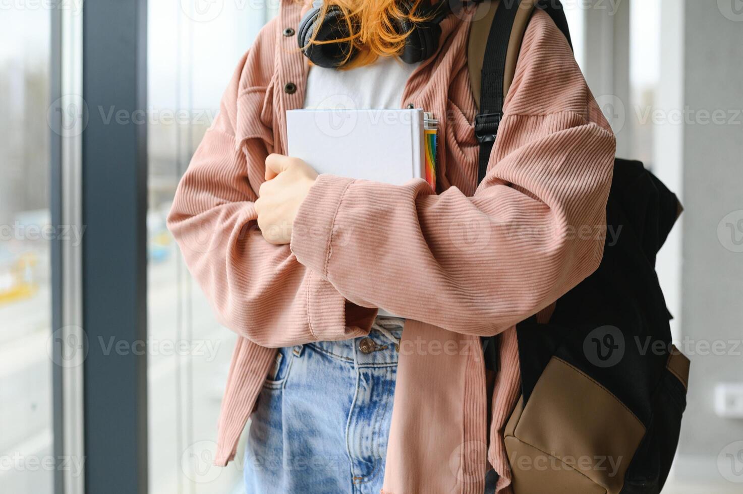 Red-haired student girl stands by the window with books and a backpack photo