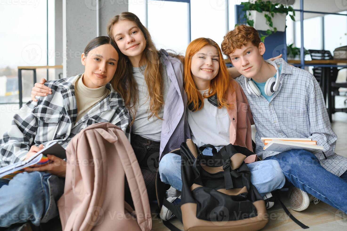 A group of cheerful student friends are sitting on the floor in a classroom photo