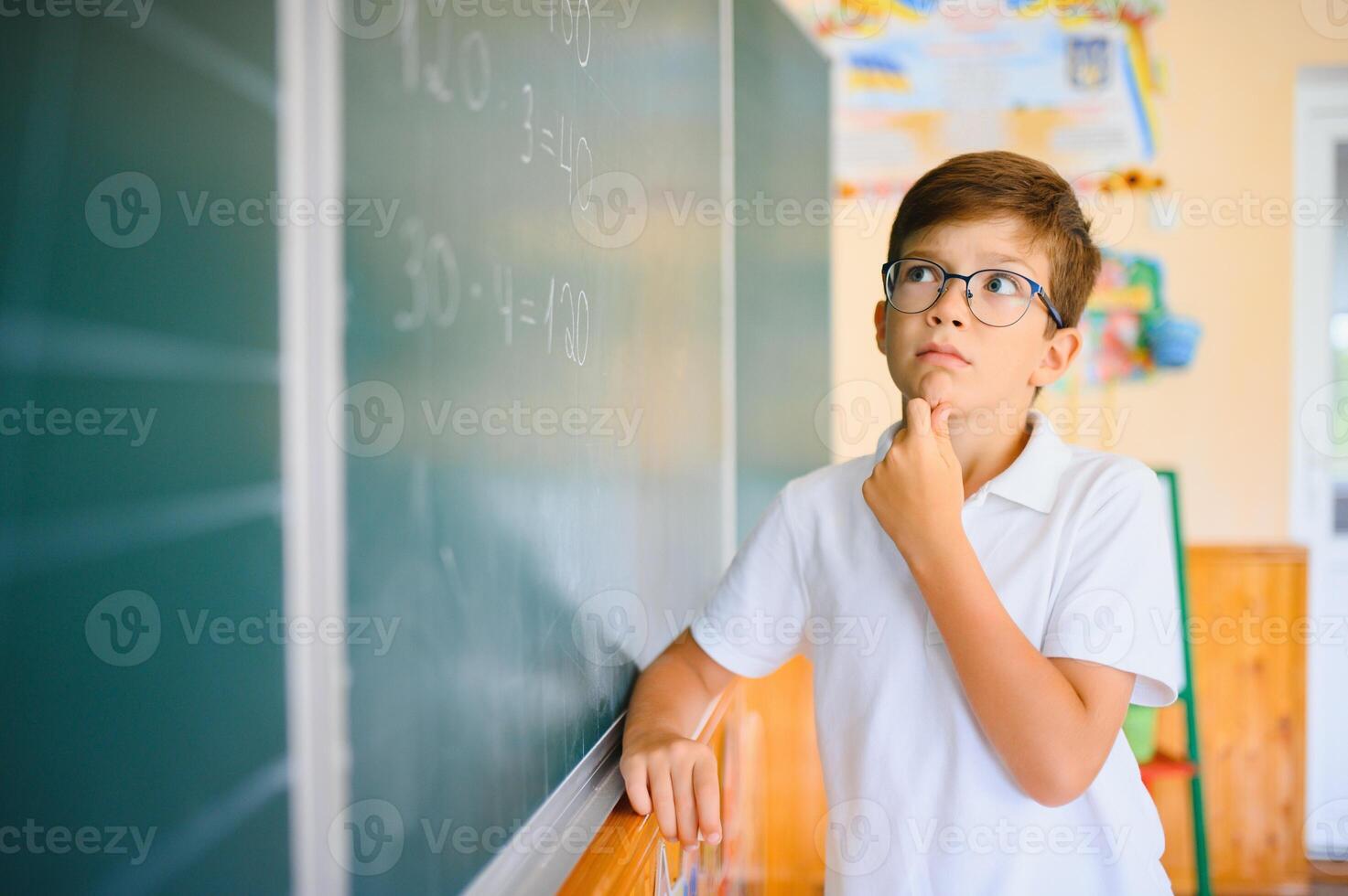 Cute little schoolboy diligent write chalk solve math problem dressed stylish uniform classroom blackboard background photo