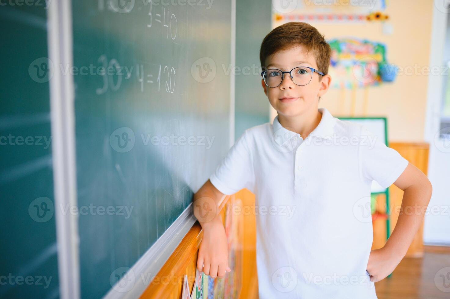 Cute little schoolboy diligent write chalk solve math problem dressed stylish uniform classroom blackboard background photo