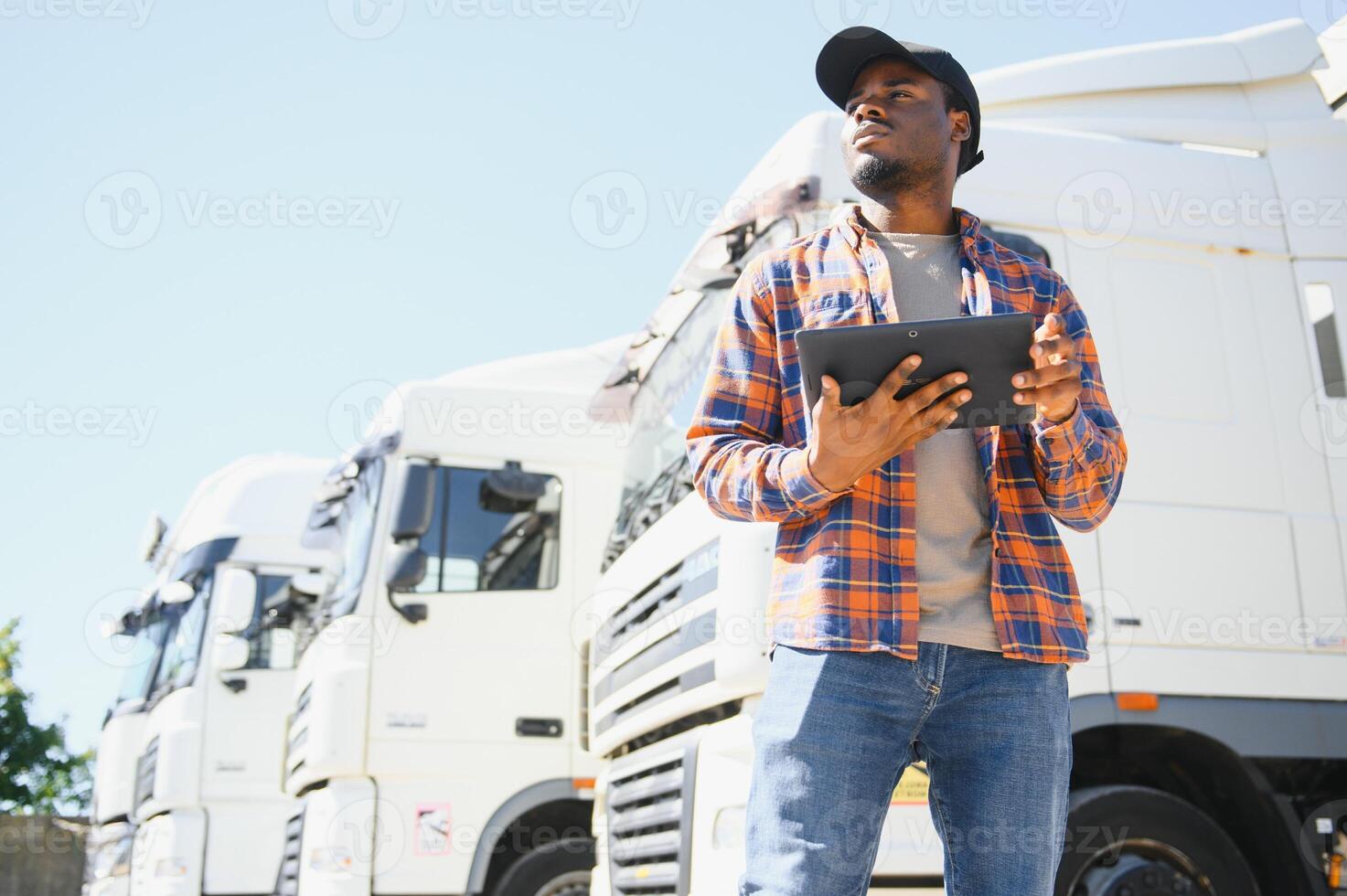 African American professional truck driver setting up navigation for destination. Checking his route on tablet computer and standing by long vehicle. Transportation service photo