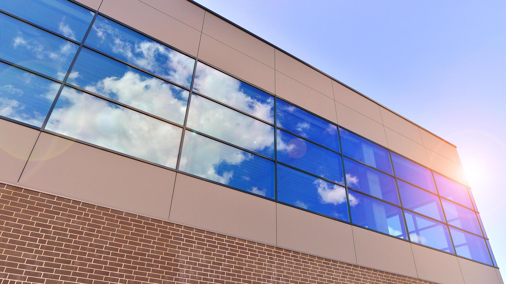 Fragment of a modern building made of steel and glass. Abstract modern commercial architecture fragment. Walls made of shiny glass and steel under blue sky. photo