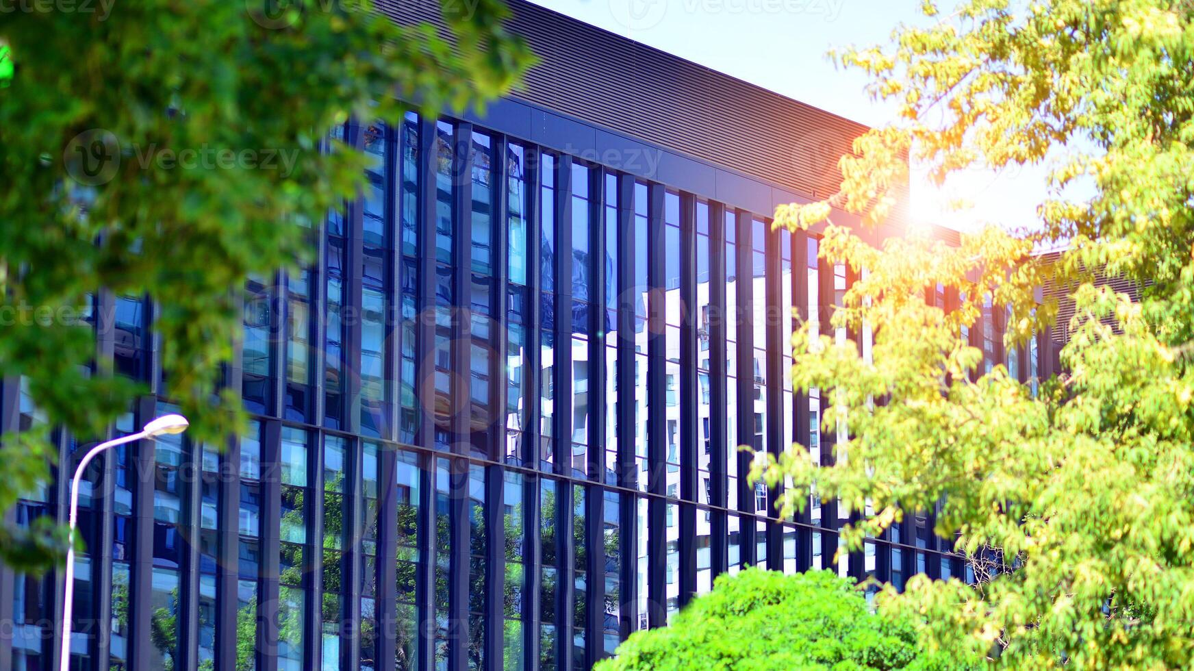City life, urban landscape and ecology. Modern office complex with glass facades and smooth lines against backdrop of green trees, concept of modern architecture. Organically building into nature. photo