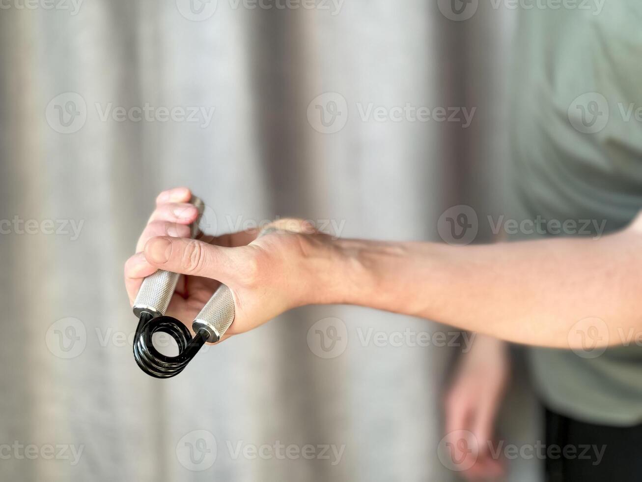 Close up of hand man holding black and silver hand expander. Focus on hand holding pen with blurred background. Concept of fitness, exercise and healthy lifestyle at home. photo