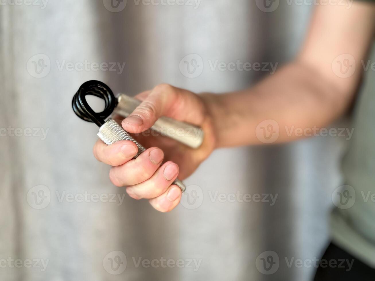 Close up of hand man holding black and silver hand expander. Focus on hand holding pen with blurred background. Concept of fitness, exercise and healthy lifestyle at home. photo