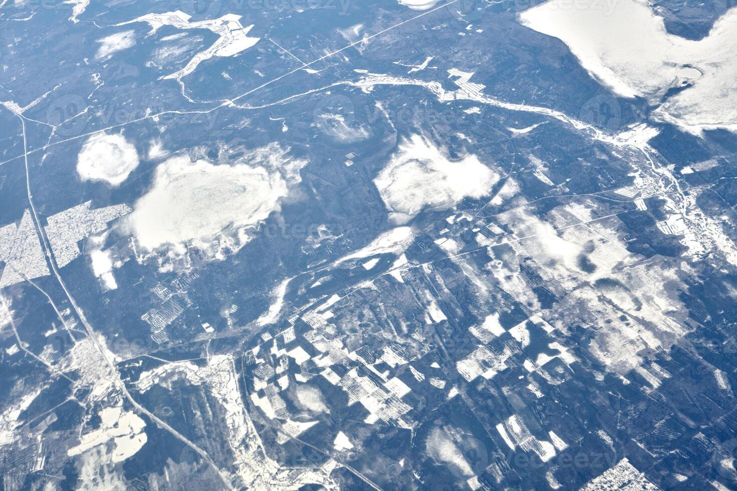 Aerial view from airplane window over clouds top to snow covered rivers, fields and roads photo