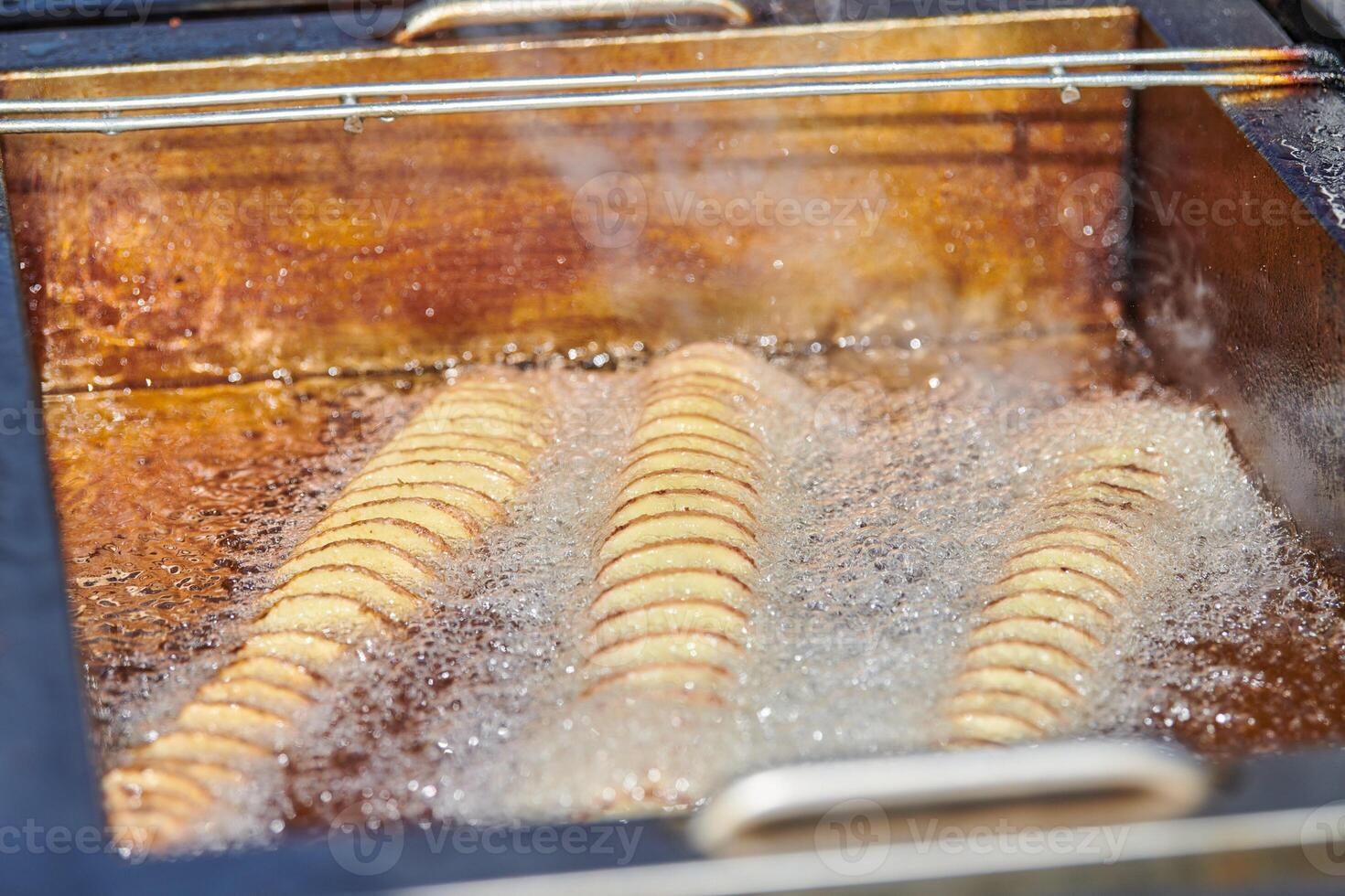 Cooking spiral fried potato in boiling oil, rich in fat and calories fast food, unhealthy delicious photo
