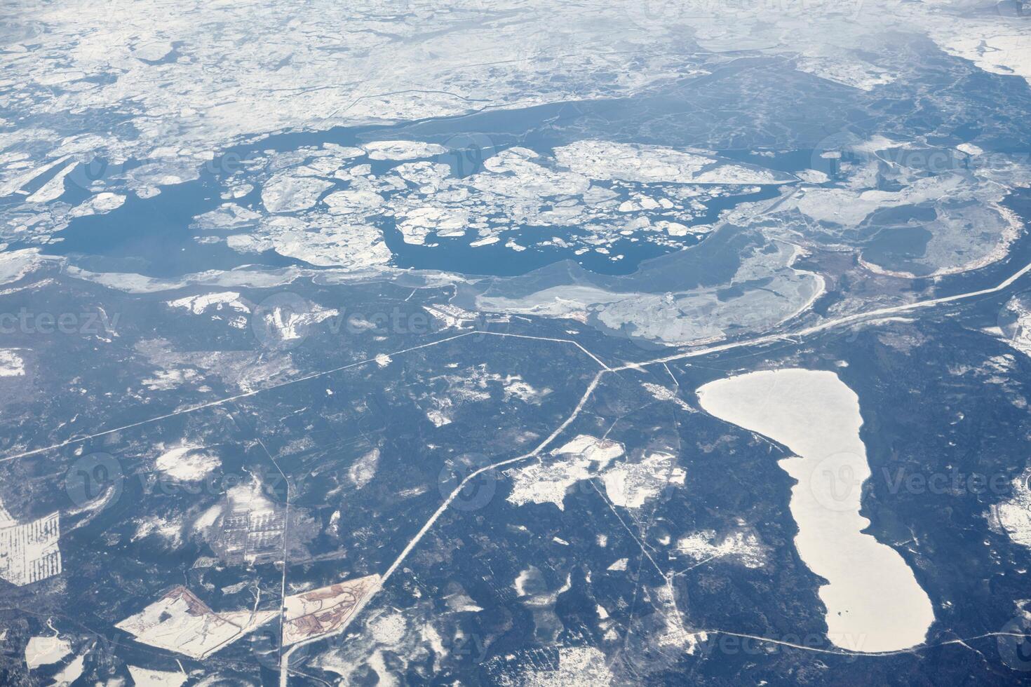 Aerial view from airplane window over clouds top to snow covered rivers, fields and roads photo