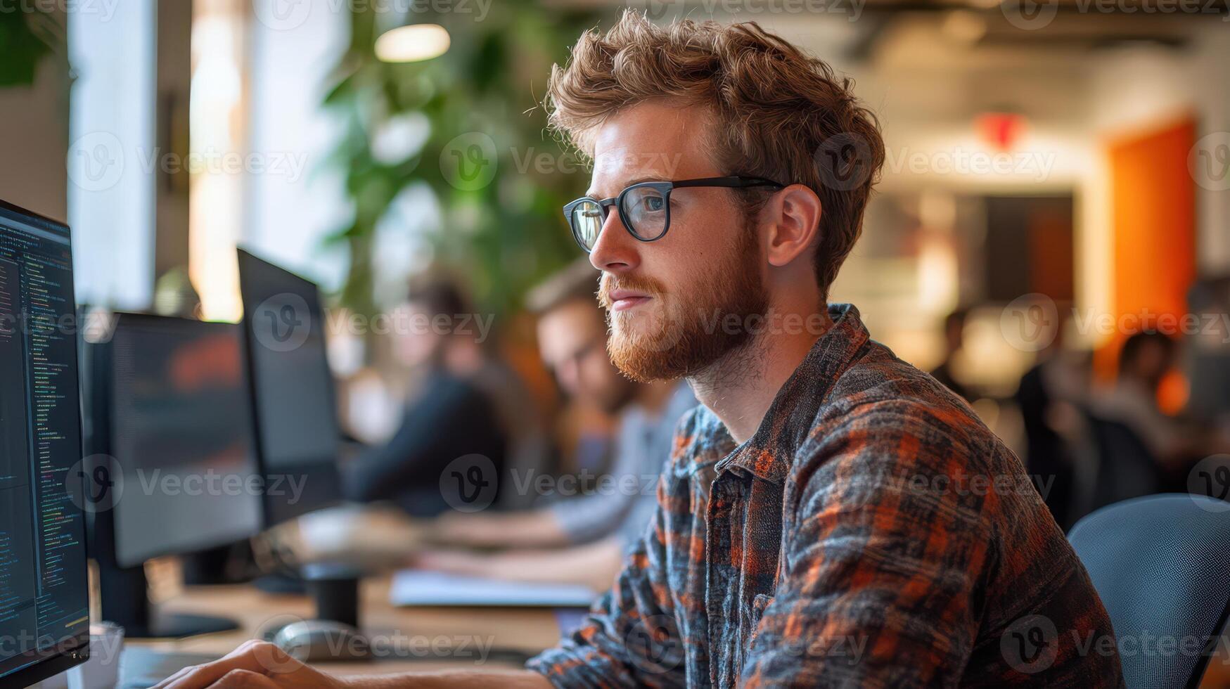 A man with glasses is sitting at a desk with a computer monitor in front of him photo