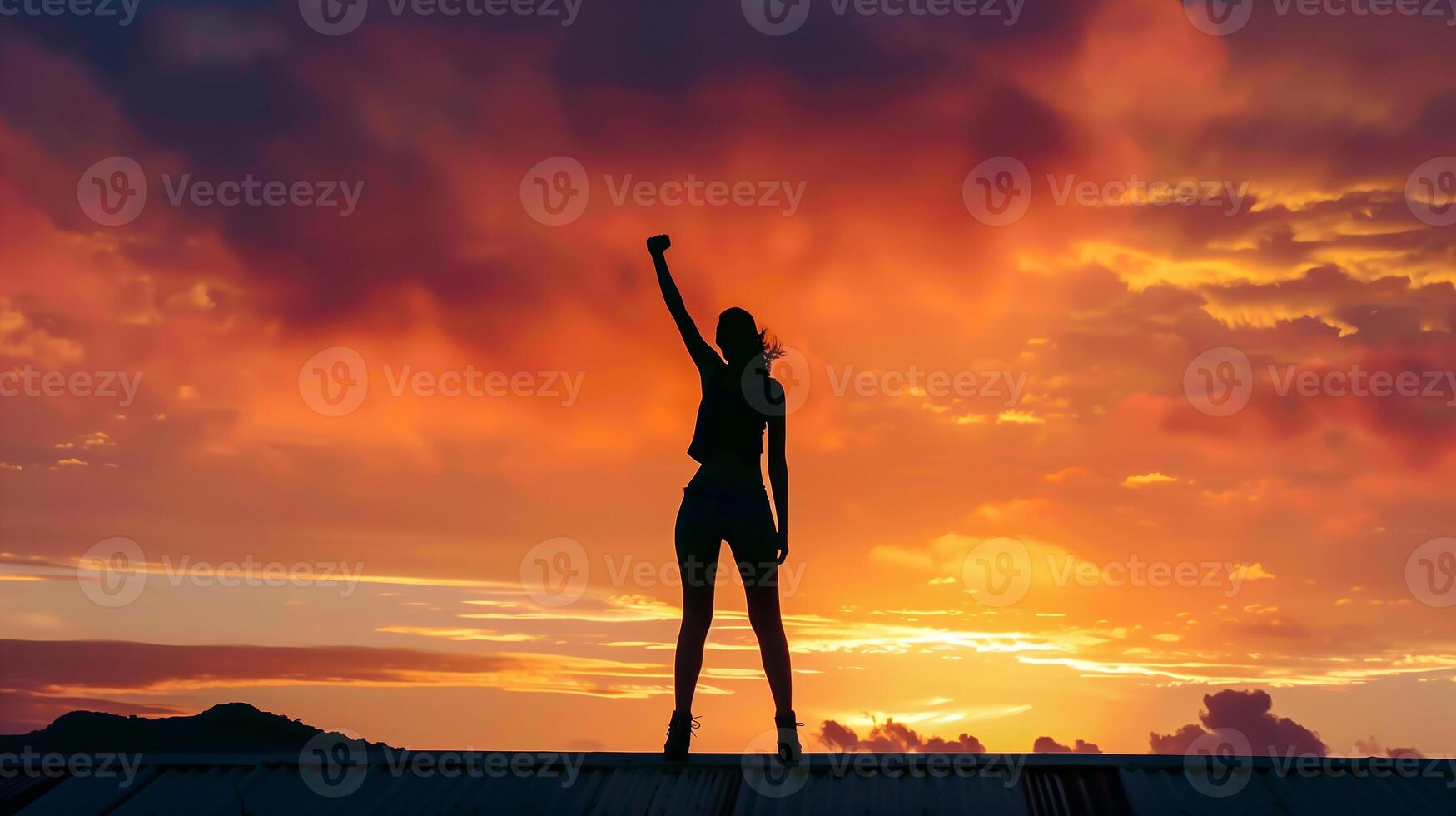 Silhouette of woman with victory and success with raised fist standing against sunset sky photo