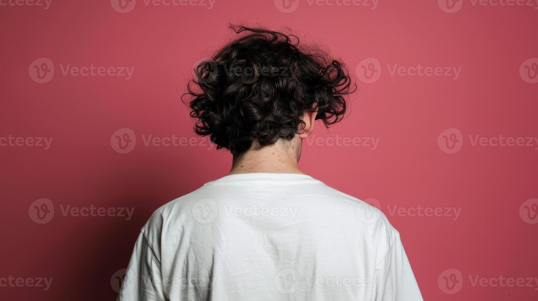 Young man with curly hair facing a pink wall in a casual setting photo