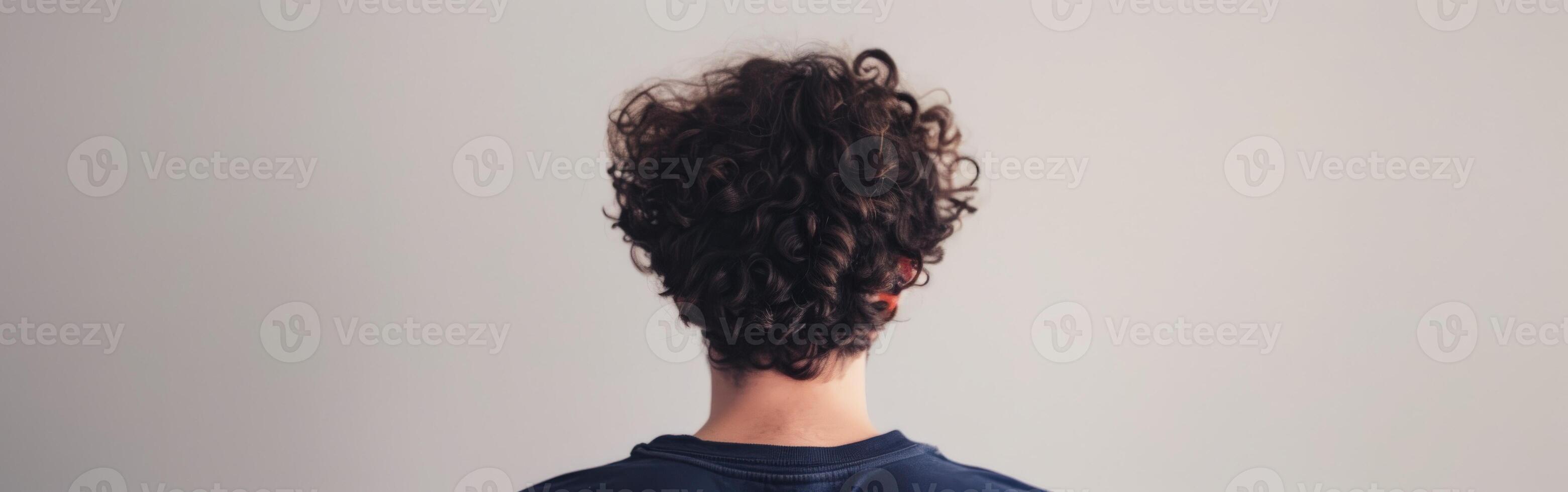 Young man with curly hair standing against a plain wall indoors photo