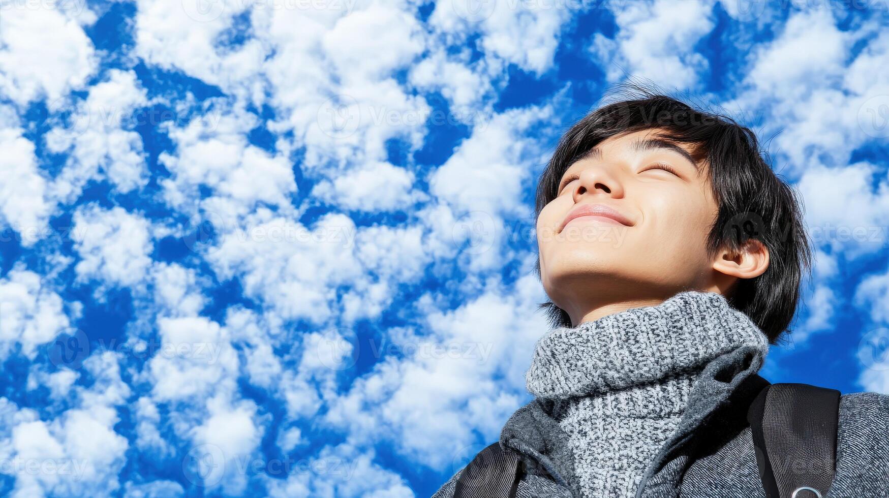 High school boy gazing at a bright blue sky with fluffy clouds photo