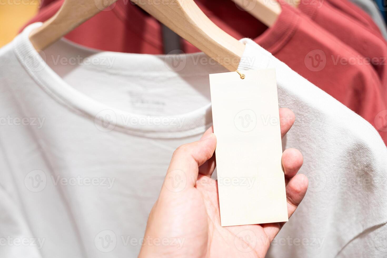 Hand holding blank paper price tag. blank tag with Clothes on a shelf in a designer clothes store. Blank for text. photo