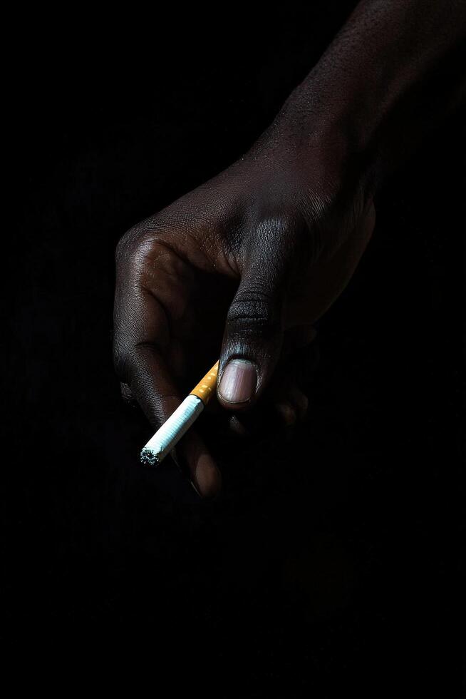 Close-up of a hand holding a cigarette against a black background photo