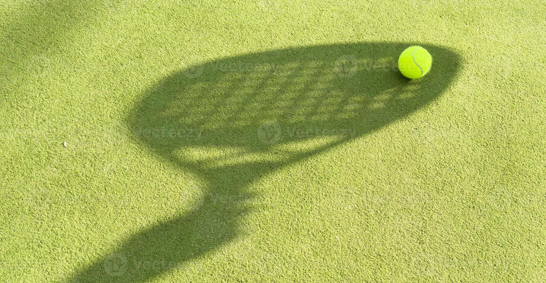 Shadow of a padel racket with a yellow ball on the green grass. photo