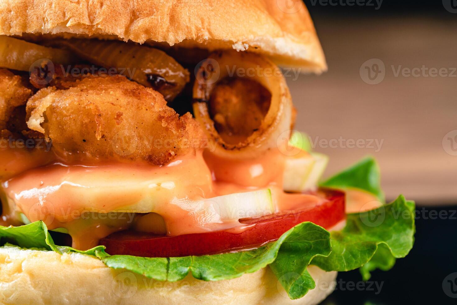 Delicious crispy fish burger with lettuce, tomato, onion ring and mayonnaise. Fish Burger with Hamburger Bun on wood background. photo