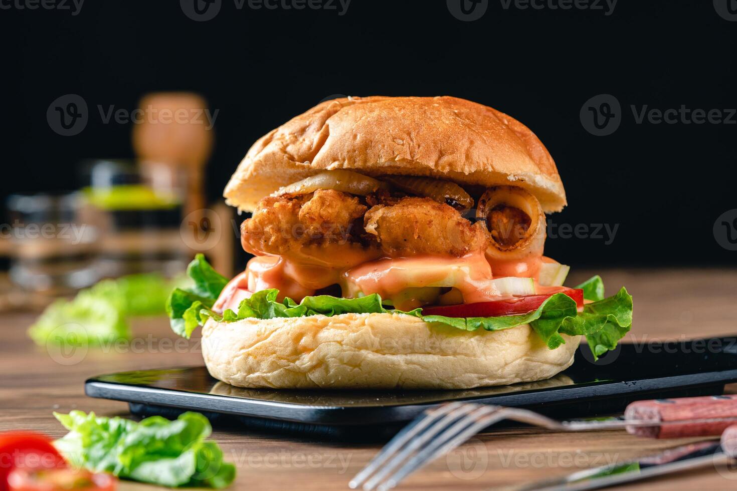 Delicious crispy fish burger with lettuce, tomato, onion ring and mayonnaise. Fish Burger with Hamburger Bun on wood background. photo