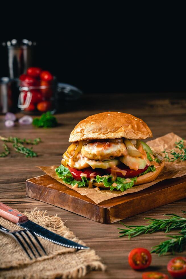 hamburger stuffed with fried egg, cucumber, tomato, mayonnaise, lettuce, onion on wood and dark background. photo