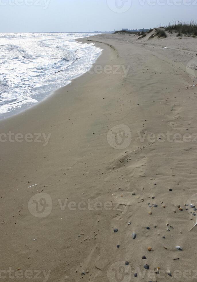 Wide sandy beach, waves with white foam roll on the shore photo