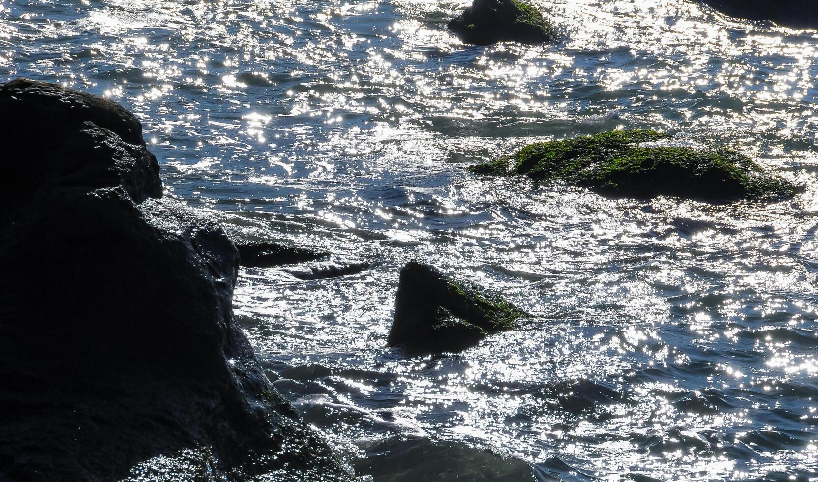 Bright reflections on the water on a sunny day among the coastal rocks near the Black Sea coast photo