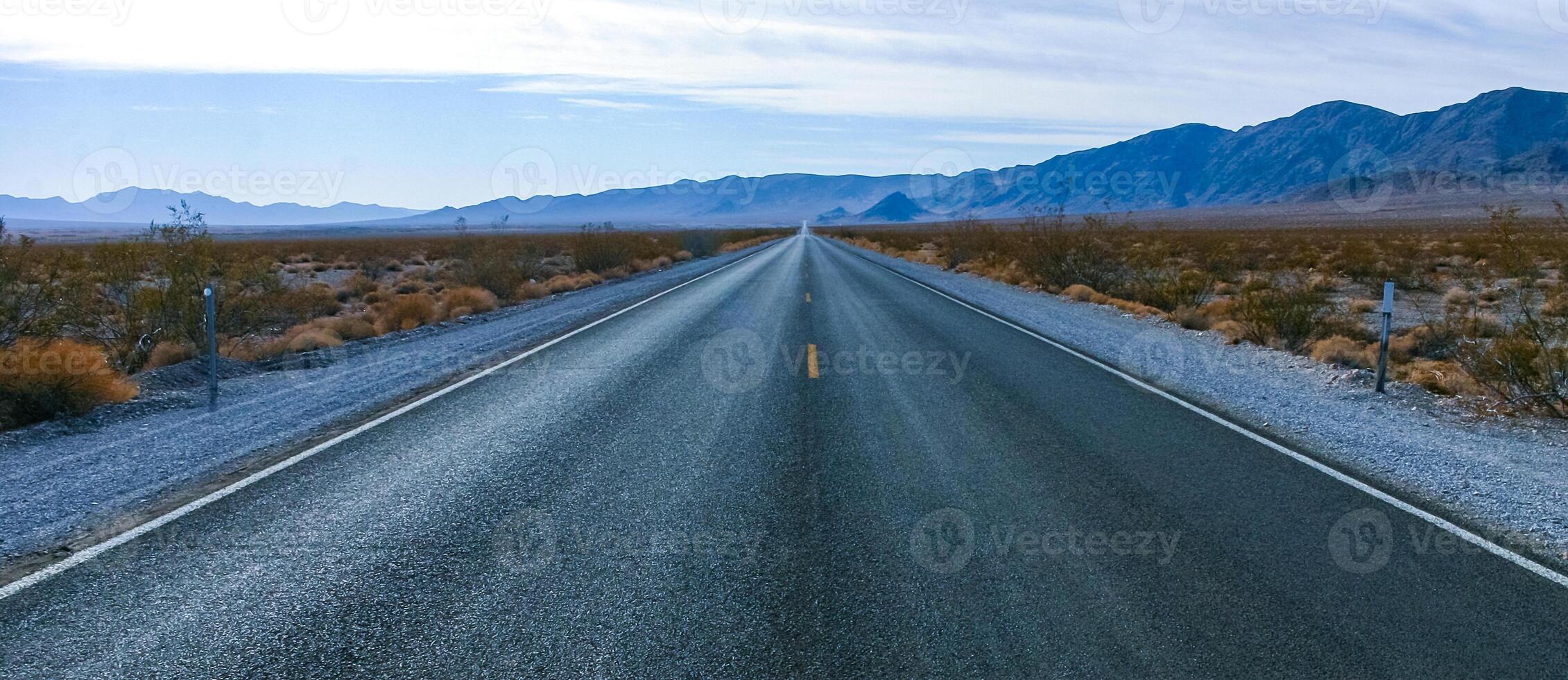 Straight asphalt road in a rocky desert in a valley towards high mountains, California photo