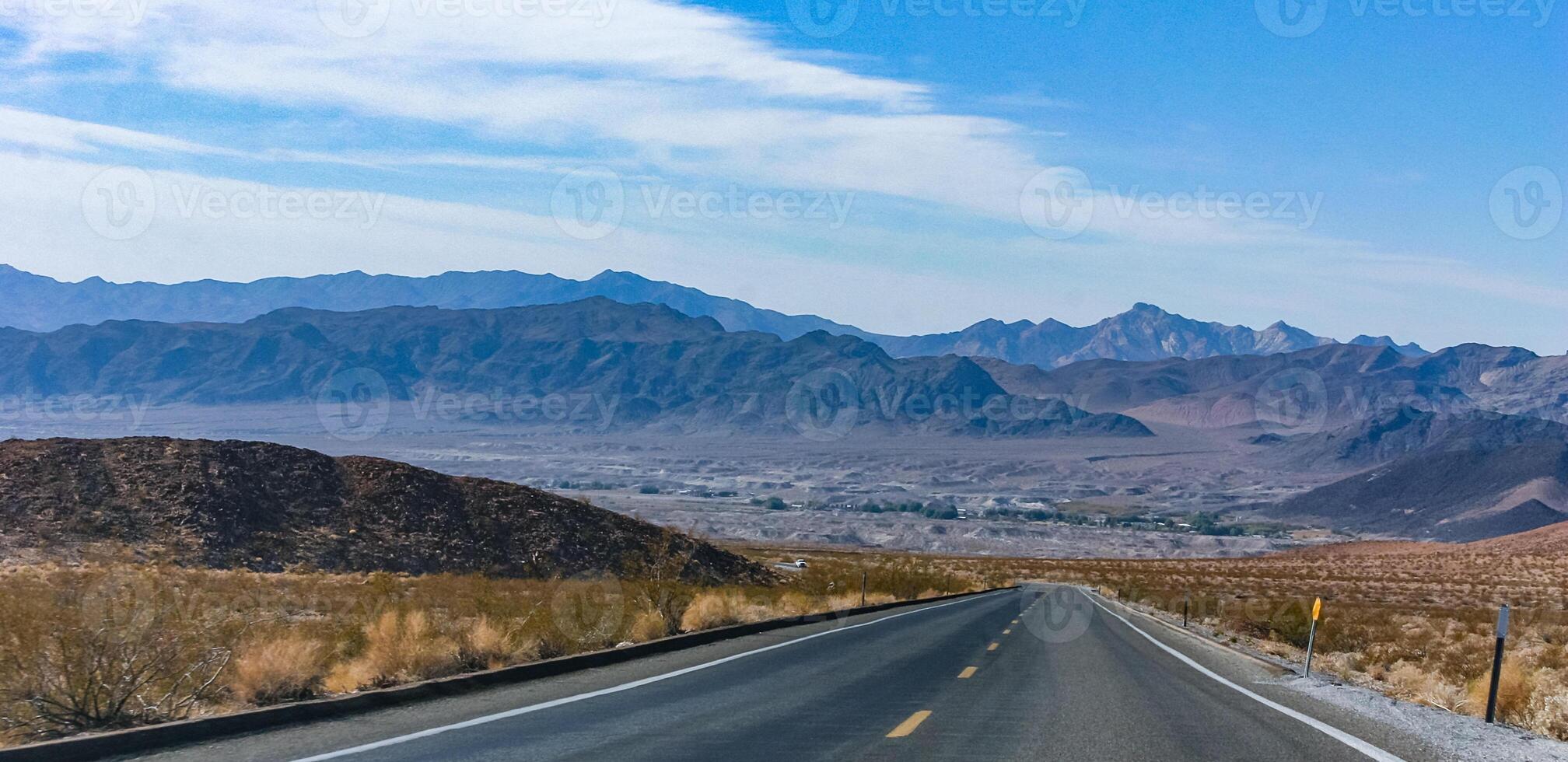 Straight asphalt road in a rocky desert in a valley towards high mountains, California photo