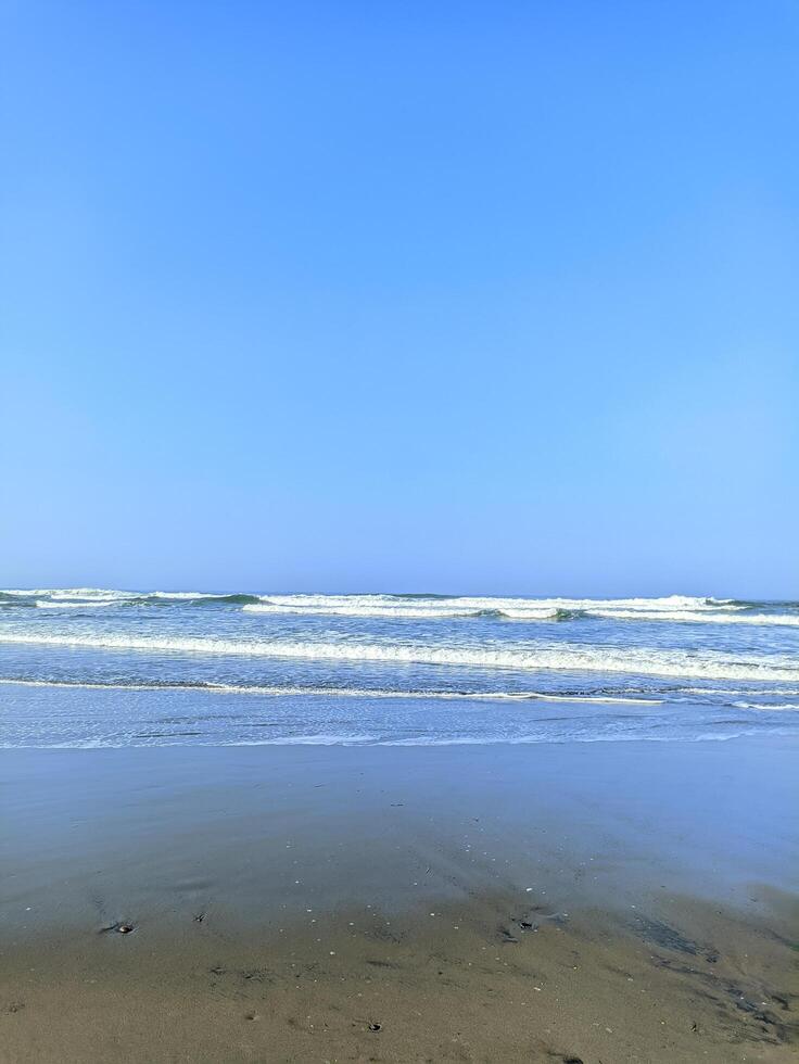 View of the beach in the morning with calm waves heading towards the coast against a clean blue sky photo
