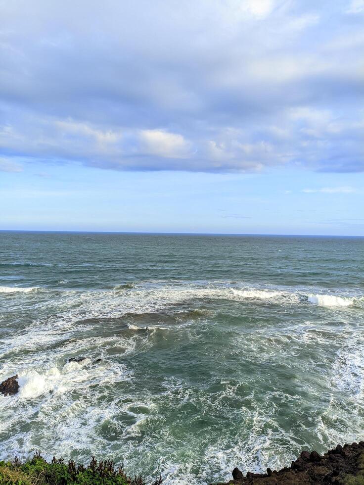 The vast blue ocean with big waves splashing water on the rocks photo