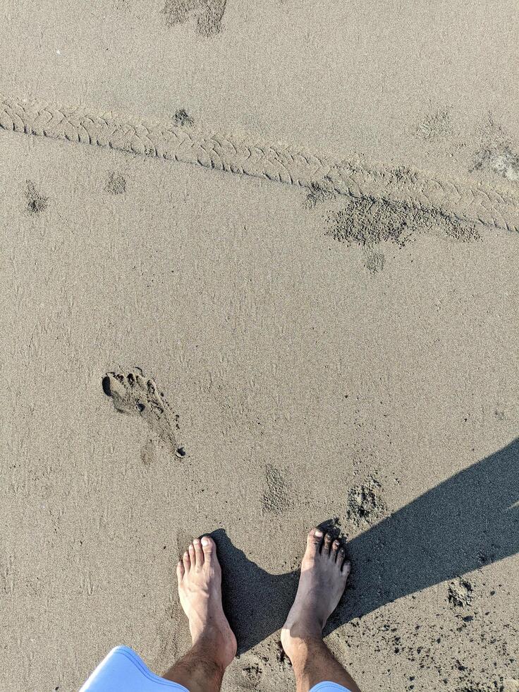 photo of a man's feet stepping on gray beach sand with his shadow