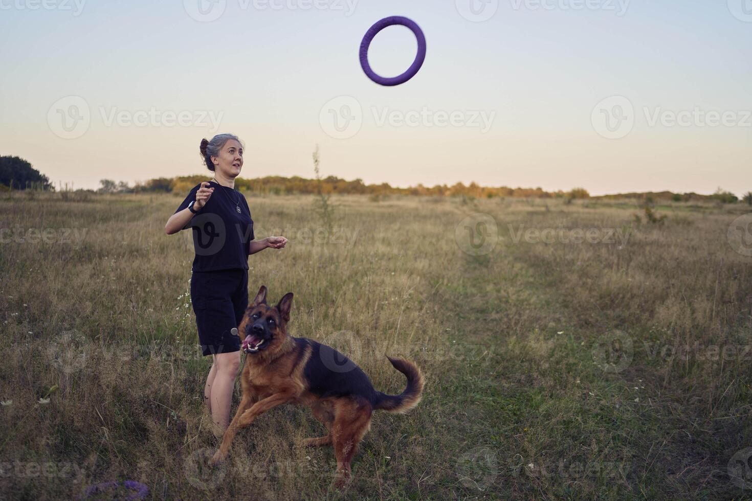 two women play in the field with a german shepherd dog toy at sunset photo