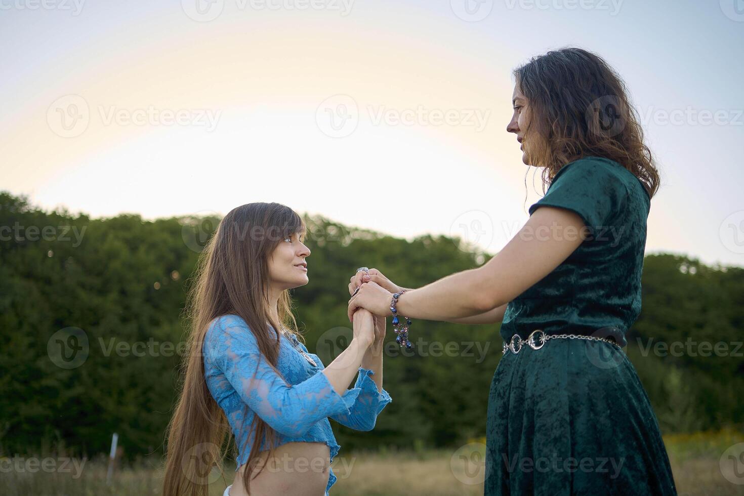 two woman in whimsical aesthetic style dress dance in a field in the summer at a sunset photo