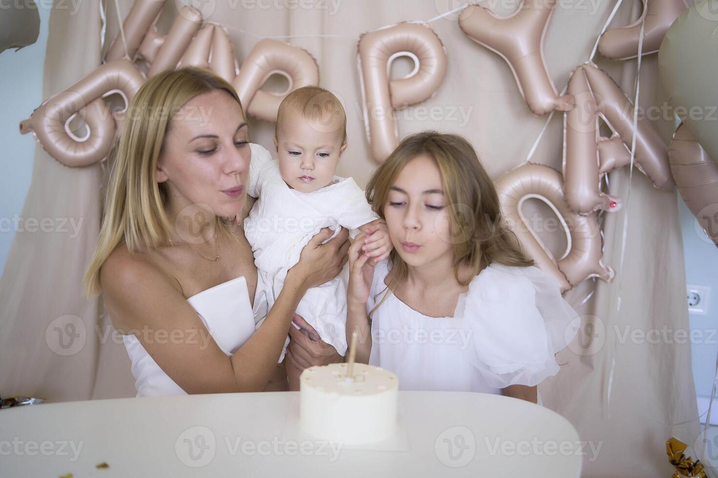 baby girl tries her first birthday cake with mom and pre-teen sister photo