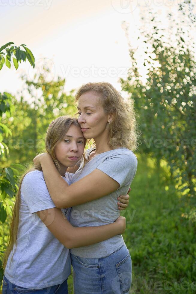 mother and teenage girls with long blond hair spend time together in the sunlit park photo