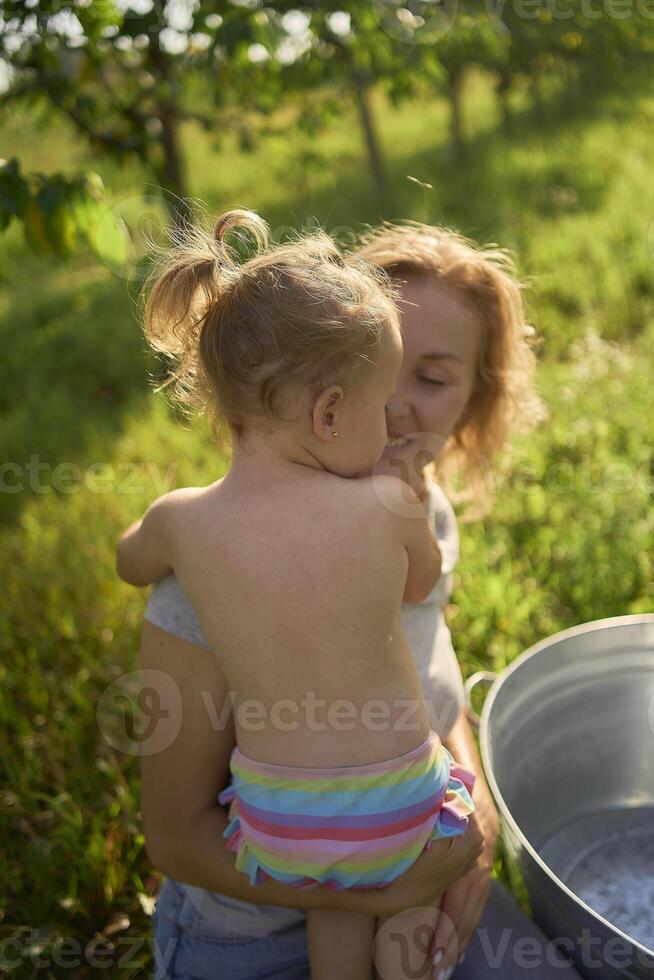mother bathes and plays with toddler in tub in garden photo