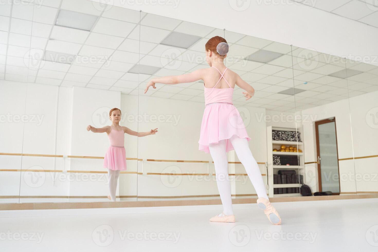 Young ballet girl at studio lesson. Training performance. Stretching exercise pose. Ballerina practice balance technique. Classical elegance fitness. Dancing costume. Pink dress, skirt photo