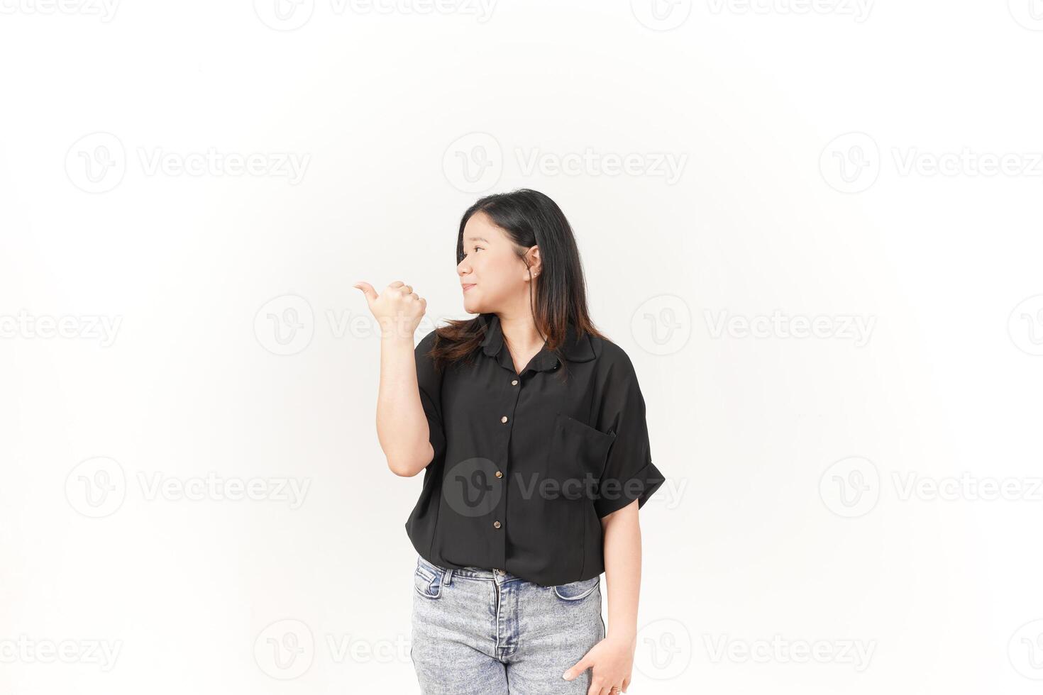 Young Asian woman pointing aside wall copy space wearing Black t-shirt and jeans isolated on white background photo