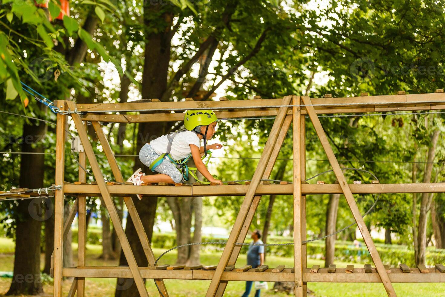 Little girl is standing on a rope, holding a rope with his hands. A child in a rope park passes obstacles photo