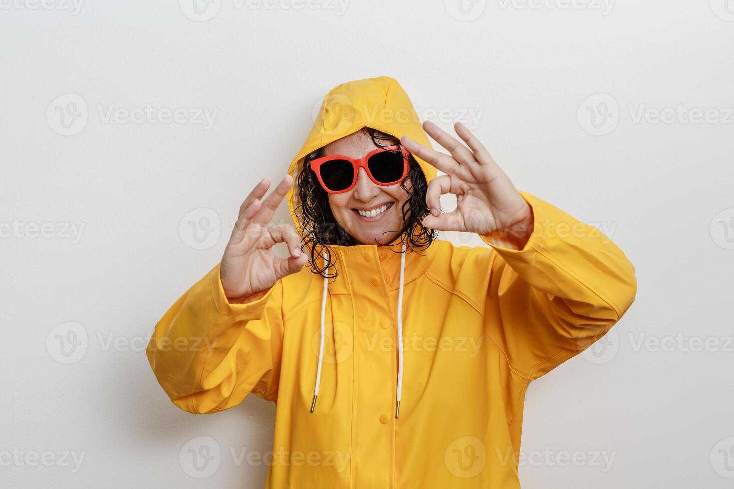 Cheerful Individual in Yellow Rain Jacket and Red Sunglasses Gesturing Okay Sign photo