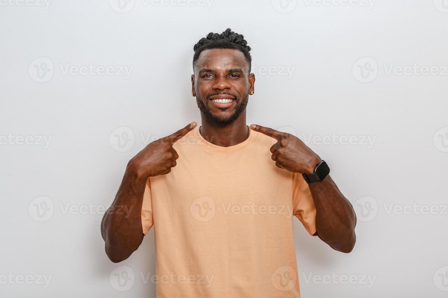 Smiling man wearing a casual peach shirt points at himself against a neutral background in a studio setting photo
