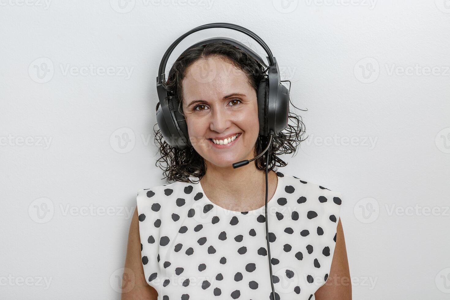 A cheerful woman with curly hair is wearing a headset with a microphone while smiling confidently photo